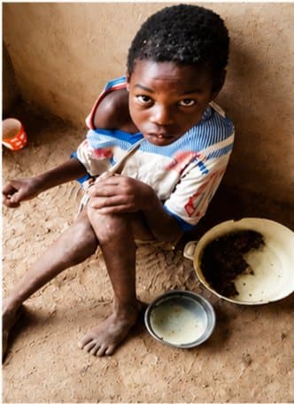 A child seated indoors beside a bowl during a support activity